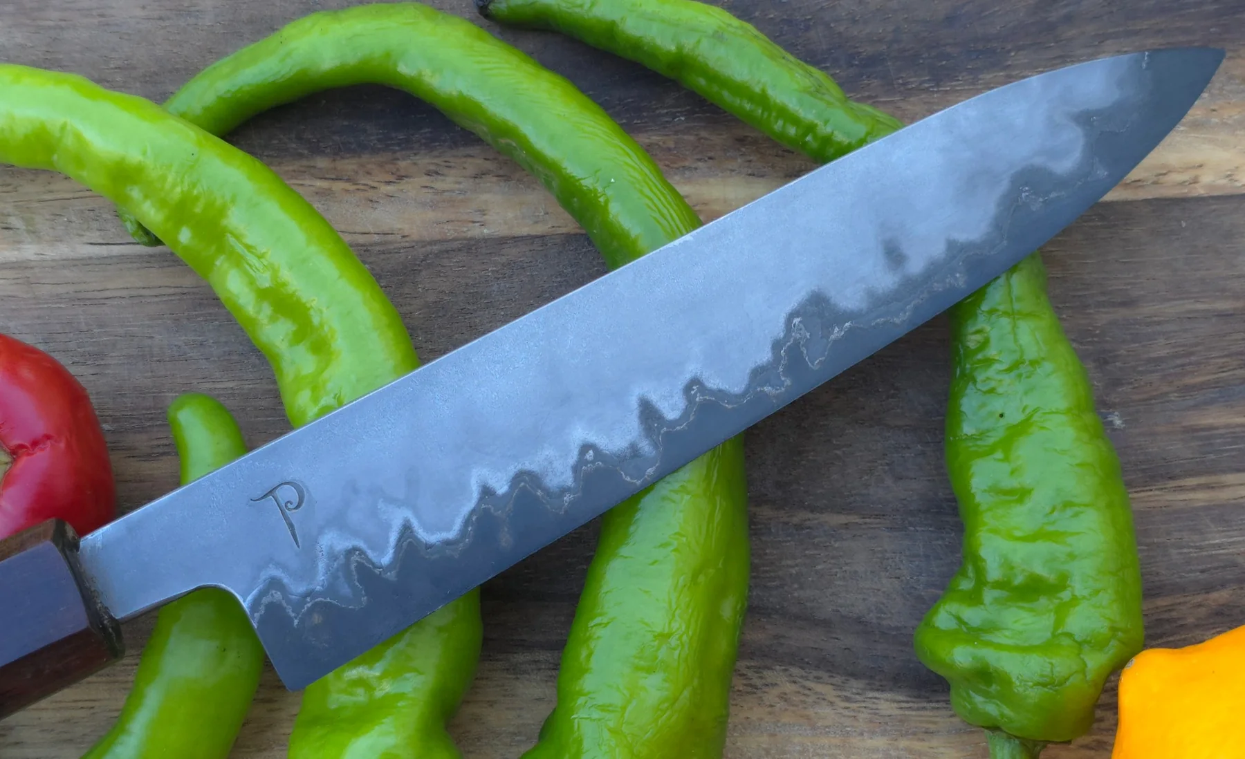 Hand-forged kitchen knife blade over fresh green peppers