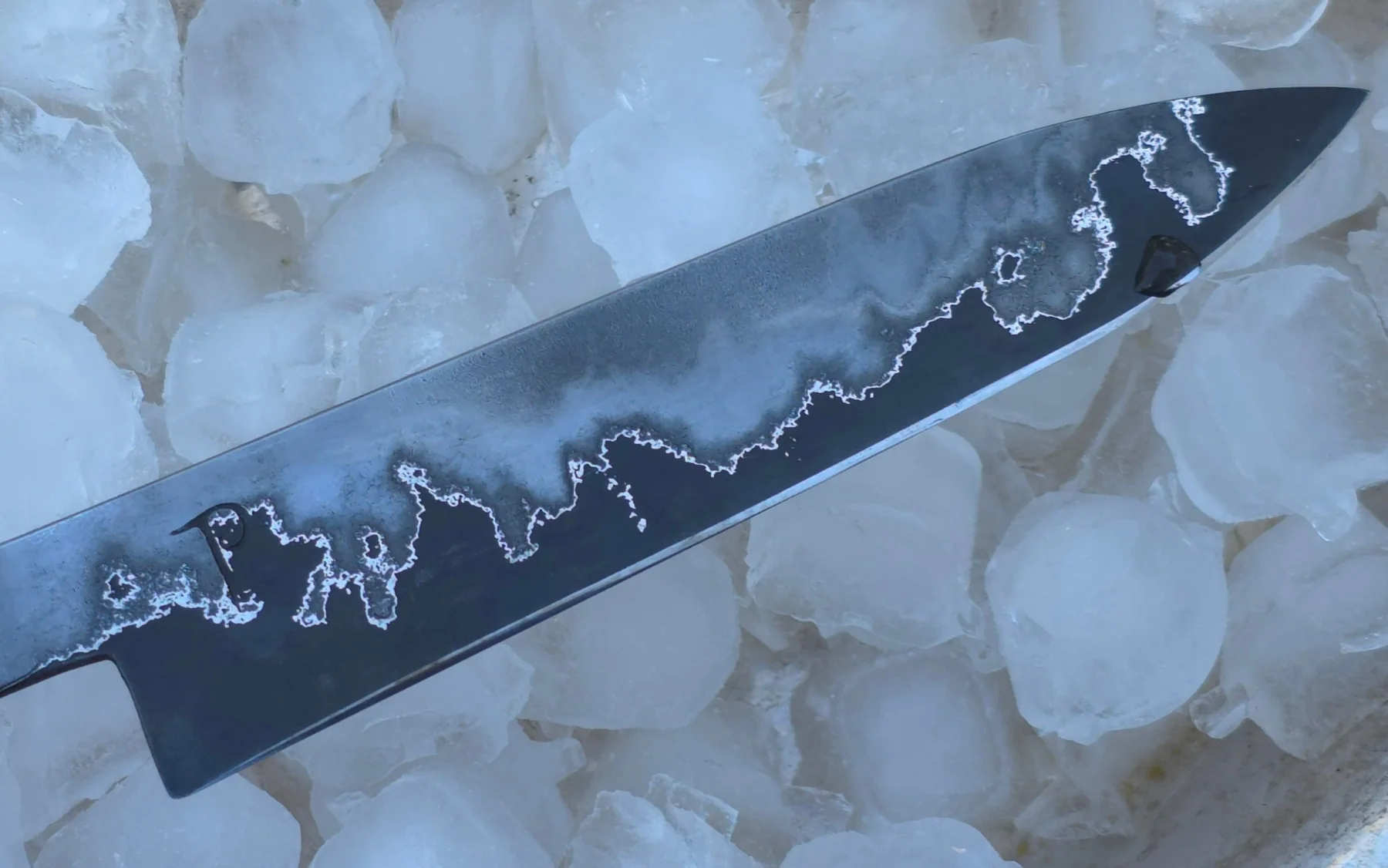 Etched hand-forged blade displayed on ice
