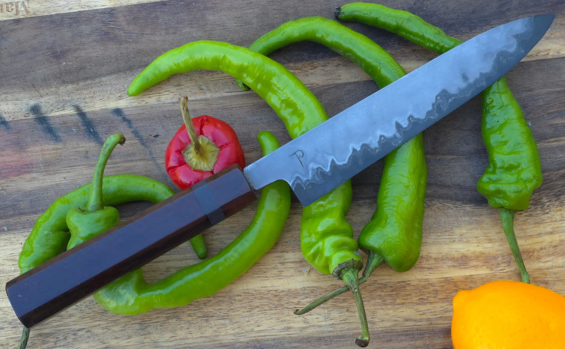Finished hand-forged kitchen knife among peppers